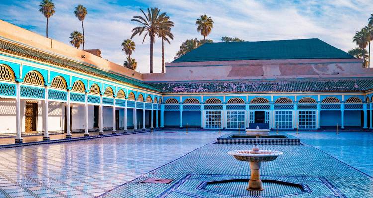 Gefliester Innenhof des Bahia-Palastes mit einem kunstvollen Brunnen, farbenfrohen Bögen und Palmen unter blauem Himmel.