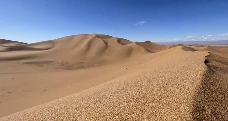 Eine weite Wüstenlandschaft mit Sanddünen unter einem klaren Himmel.