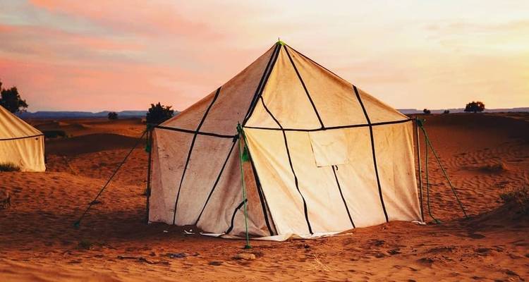 Eenvoudige witte canvastent opgezet op roodachtig zand bij kleurrijke woestijnzonsondergang