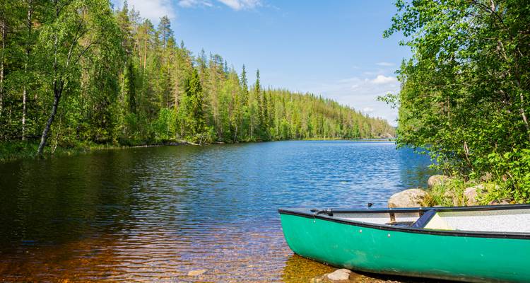 Kanu an einem bewaldeten Seeufer unter blauem Himmel.