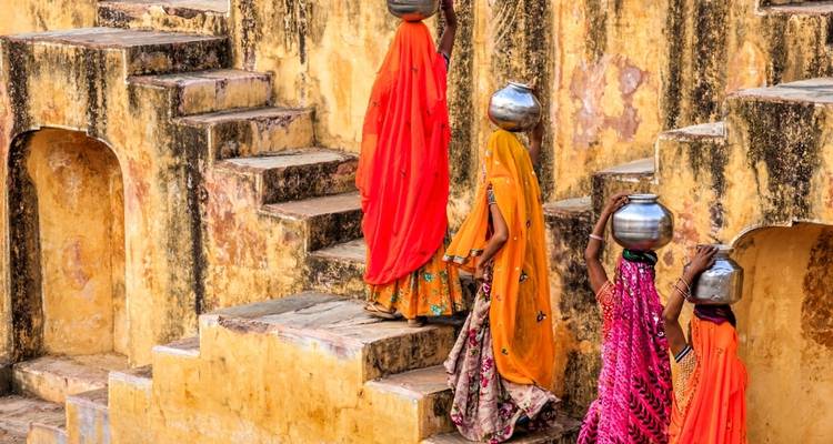 Women in colorful dresses carrying pots on their heads walking up stone steps.