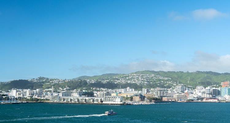 Vista panorámica del paisaje urbano de Wellington y las colinas a través de un puerto turquesa con un ferry dejando una estela blanca.
