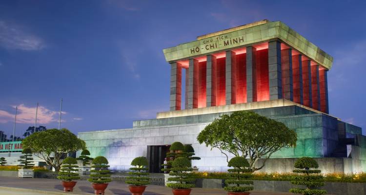 Le Mausolée illuminé de Ho Chi Minh se dresse majestueusement au crépuscule avec des bonsaïs entretenus au premier plan.