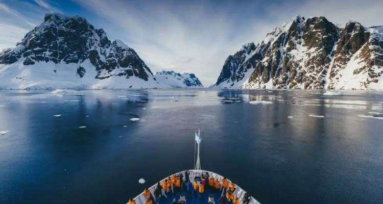 Un navire d'expédition fend les eaux glaciales calmes entouré de pics enneigés imposants et de glaciers.