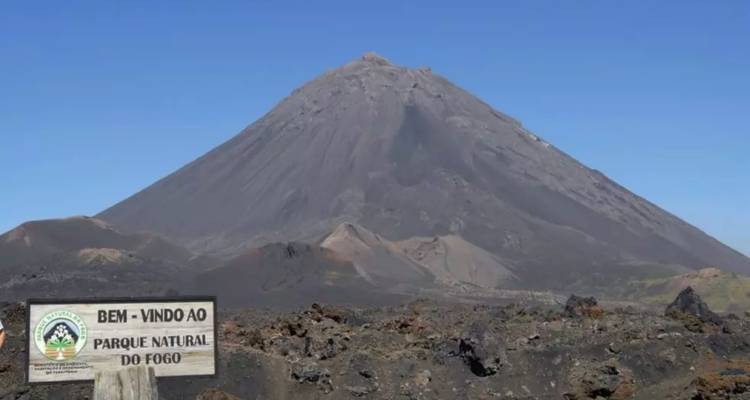 Le pic volcanique noir du Pico do Fogo s'élève au-dessus d'un paysage lunaire avec un panneau de bienvenue au parc national.
