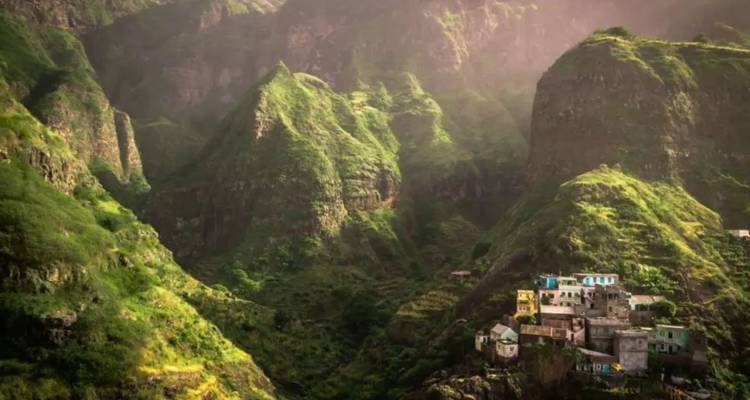 Montagnes vertes spectaculaires et vallées escarpées avec un petit village accroché au flanc de la colline dans une lumière douce.