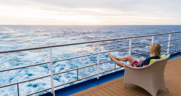 Ein Passagier entspannt sich in einem Liegestuhl und beobachtet, wie sich die Heckwelle des Schiffes bei Dämmerung über das offene Meer erstreckt.
