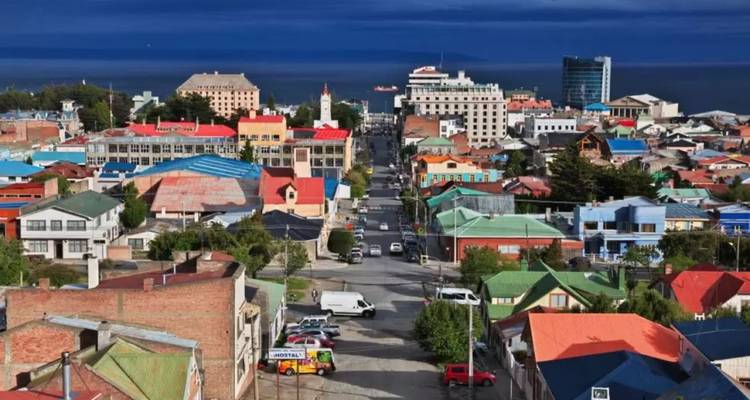 Colorful downtown grid of Punta Arenas with dramatic dark clouds and a distant channel.