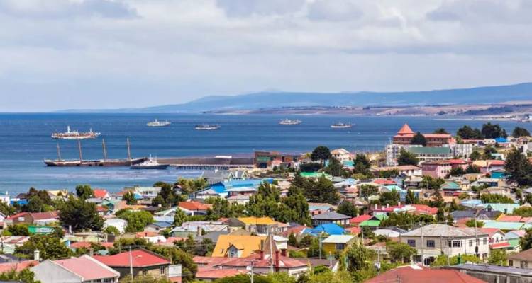 Seaside town with colorful roofs, ships anchored in a wide blue bay and rolling hills beyond.