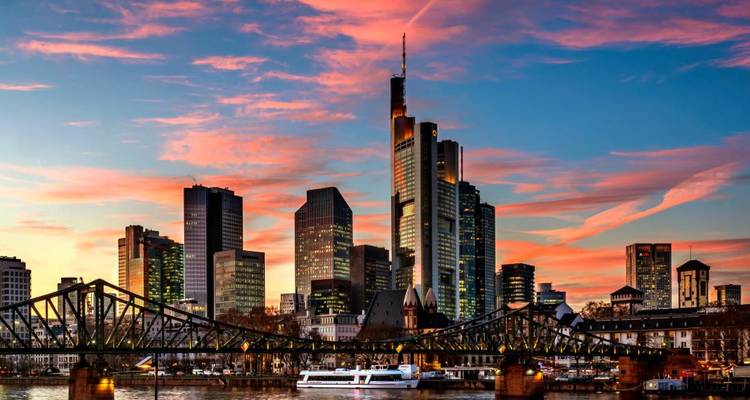 Modern city skyline with tall glass skyscrapers and a bridge reflected at vibrant sunset.