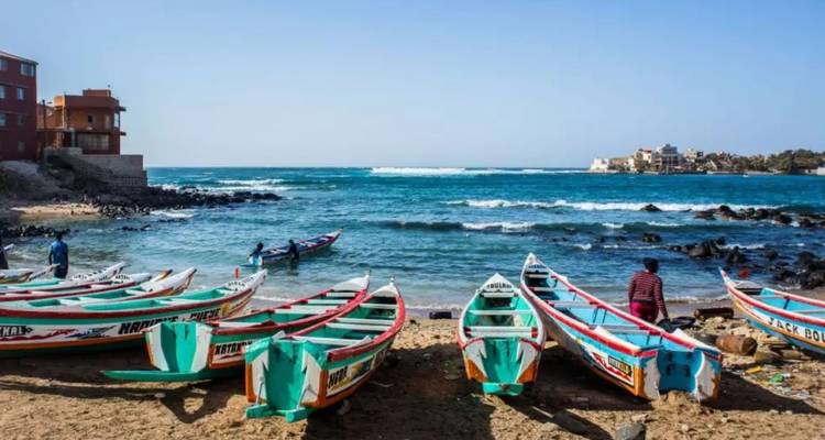 Bateaux de pêche en bois colorés tirés sur une plage de sable avec des vagues turquoise de l'Atlantique et quelques pêcheurs travaillant le long du rivage
