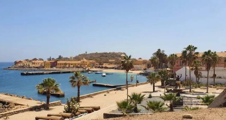 Établissement côtier historique avec des bâtiments coloniaux pastel et des palmiers surplombant une baie bleue calme et une petite jetée