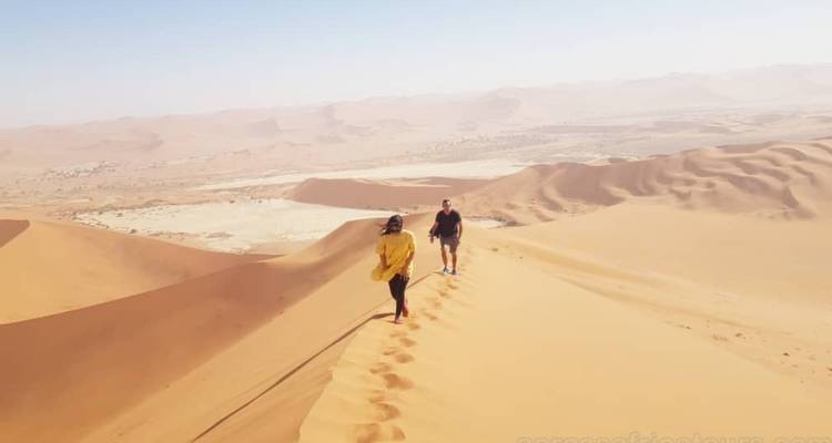 Two people hiking along a sand dune ridge.