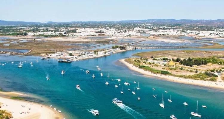 Luchtfoto van een helder blauwe lagune met boten die een kustplaatsje in Portugal binnenvaren en zoutpannen ernaast