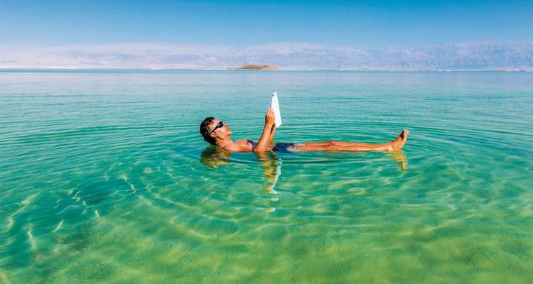 Mann liest ein Buch, während er im Toten Meer treibt.
