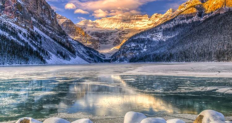 Lago Louise congelado reflejando las Montañas Rocosas cubiertas de nieve bañadas en la cálida luz del amanecer con un primer plano helado.