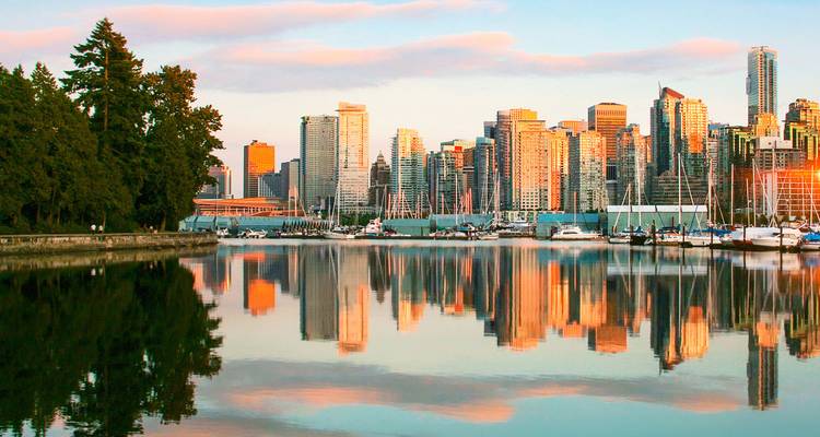 Skyline de Vancouver se reflétant sur les eaux calmes du port à l'heure dorée avec des bateaux amarrés dans la marina.
