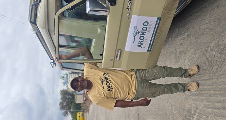 Safari-Führer, der neben einem Land Cruiser mit dem Firmenlogo lächelt.