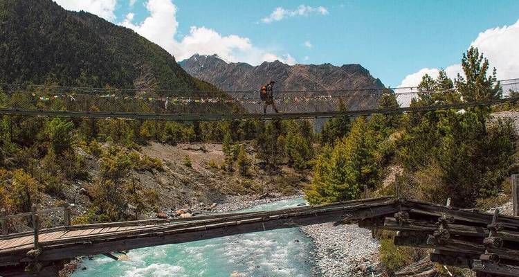 Personne marchant sur un pont élevé au-dessus d'une rivière avec des montagnes.