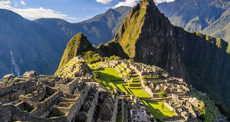 Vue panoramique emblématique des terrasses de la citadelle du Machu Picchu encadrées par les pics andins imposants sous un ciel bleu.