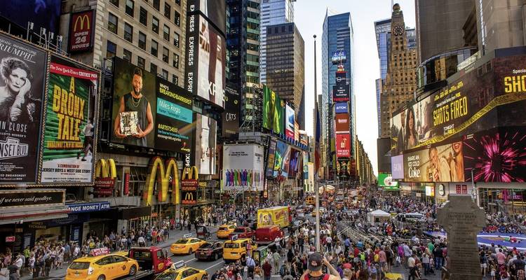 Busy and vibrant Times Square filled with tourists, signs, and yellow taxis.
