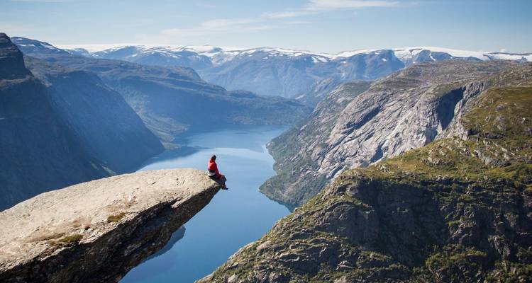 Un senderista se sienta en el dramático acantilado de Trolltunga muy por encima de un fiordo azul profundo.