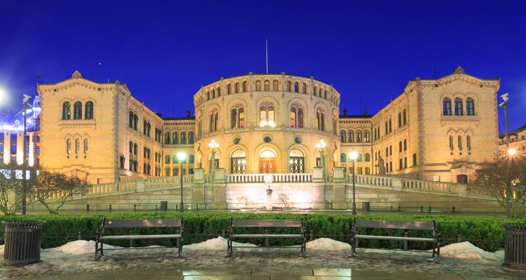 El edificio del parlamento Stortinget de Oslo brilla con calidez contra un profundo cielo azul al atardecer.