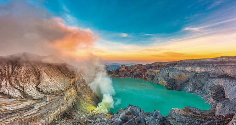 A stunning volcanic crater with vibrant turquoise water and rising steam at sunrise.