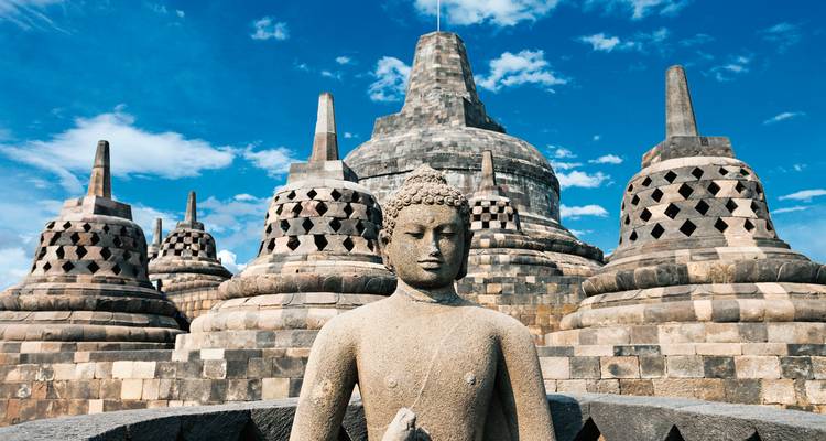 Gros plan du Temple de Borobudur avec une statue de Bouddha et des stupas par une journée ensoleillée.