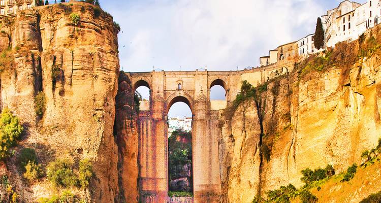 The spectacular Puente Nuevo stone bridge spans a deep gorge in Ronda under a partly cloudy sky.