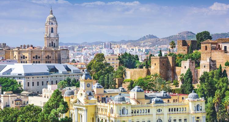 Panorama of Málaga city with its cathedral tower and Alcazaba fortress amid urban sprawl and hills.