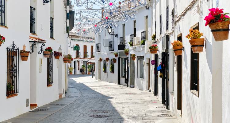 Narrow whitewashed street of Frigiliana adorned with potted flowers and decorative lights.