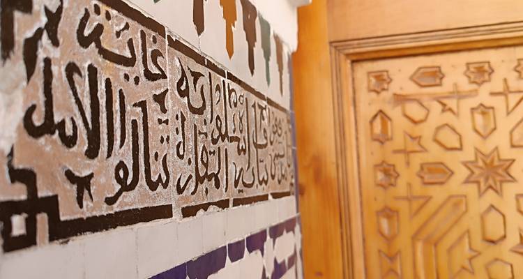 Script arabe décoratif sur un mur en mosaïque à côté d'une porte en bois.