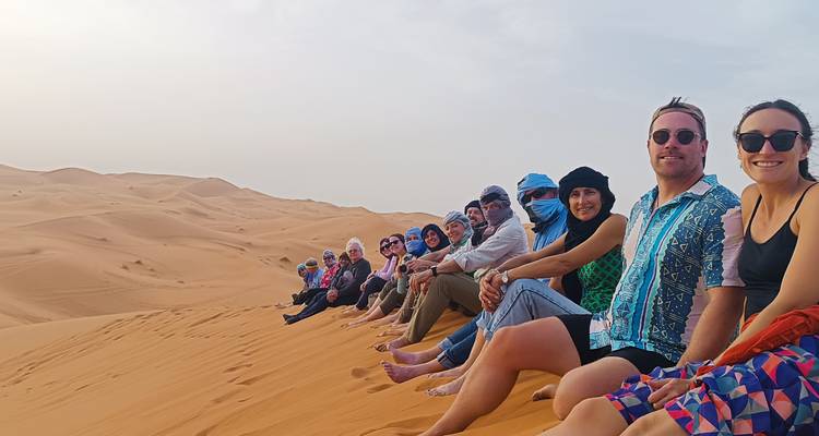 Groupe de personnes assises sur des dunes de sable profitant de la vue.