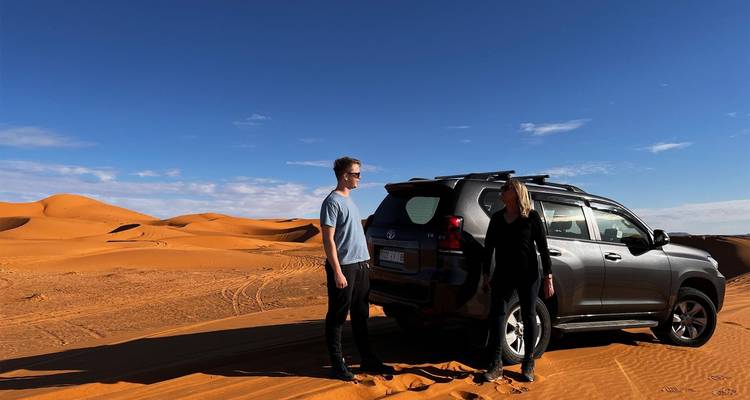 Zwei Personen neben einem Auto in einer Wüstenlandschaft.