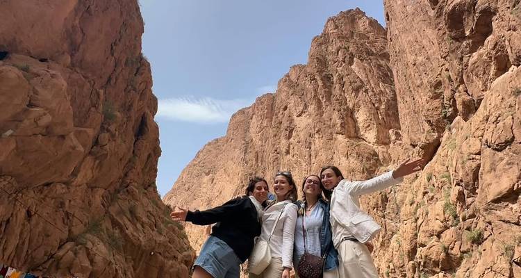 Vier Frauen lächeln und posieren in einer canyonähnlichen Umgebung.