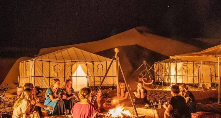 Campfire gathering with people near tents at night in the desert.