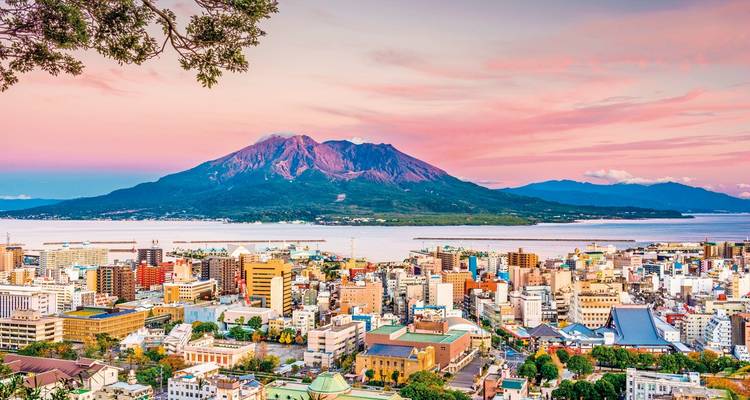 Stadsgezicht met een vulkanische berg op de achtergrond bij zonsondergang.