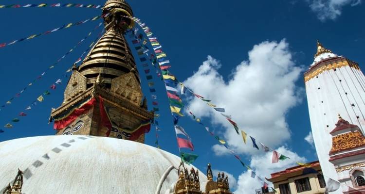 Swayambhunath Stupa with prayer flags against a blue sky.
