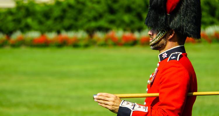 Garde cérémonielle en uniforme rouge vif et bonnet à poil marchant avec bâton.