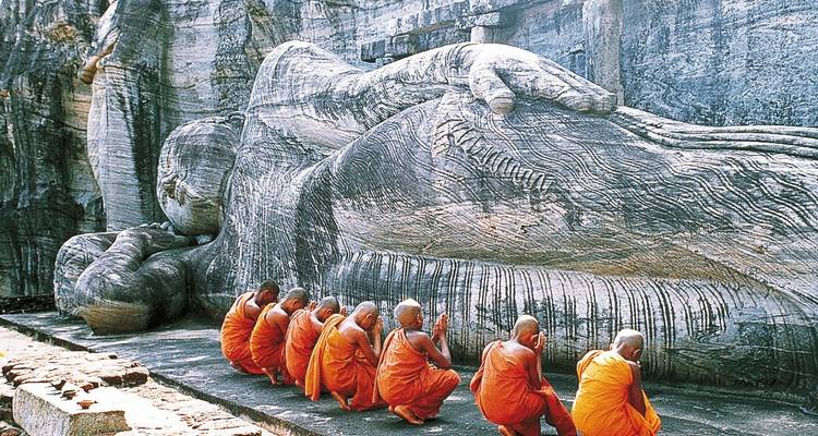 Line of monks in orange robes praying before a massive reclining stone Buddha statue