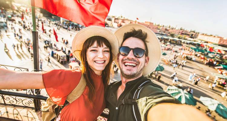 Deux personnes souriantes posant avec un drapeau au-dessus d'un marché animé.