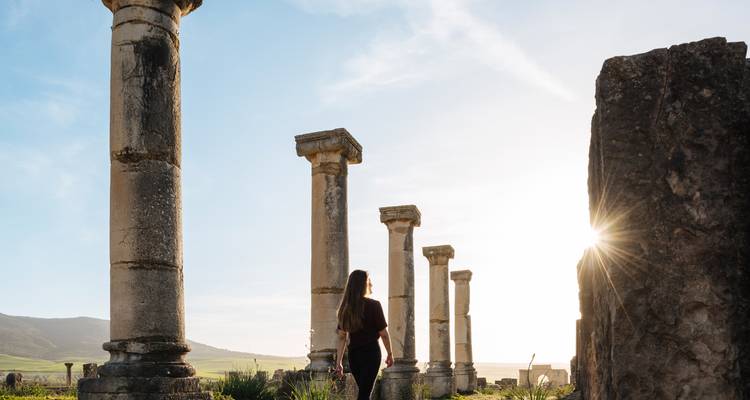 Femme marchant à travers les colonnes romaines antiques au lever du soleil.