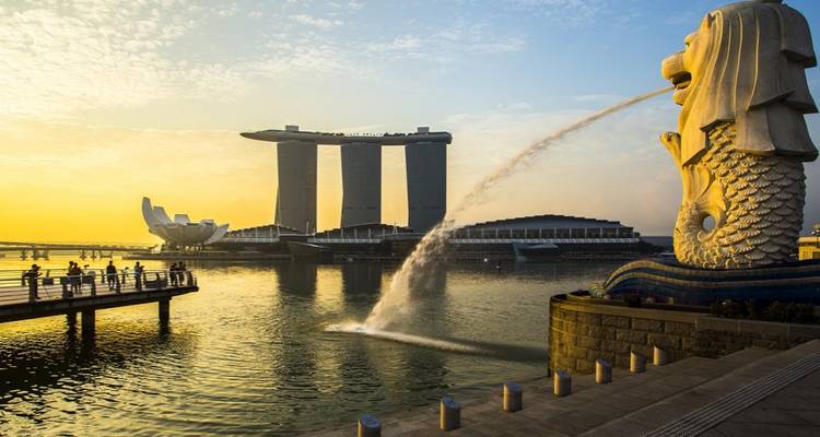 Der ikonische Merlion-Brunnen speit Wasser in Richtung der Marina Bay Sands Skyline unter einem leuchtenden Sonnenaufgang.