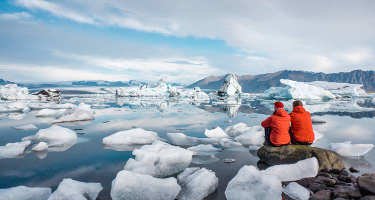 Dos personas en chaquetas rojas se sientan entre icebergs junto al agua.