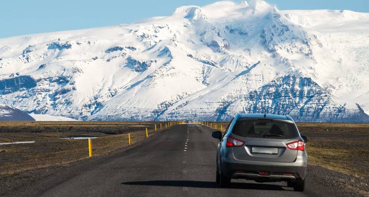 Coche conduciendo hacia un paisaje de montañas nevadas.