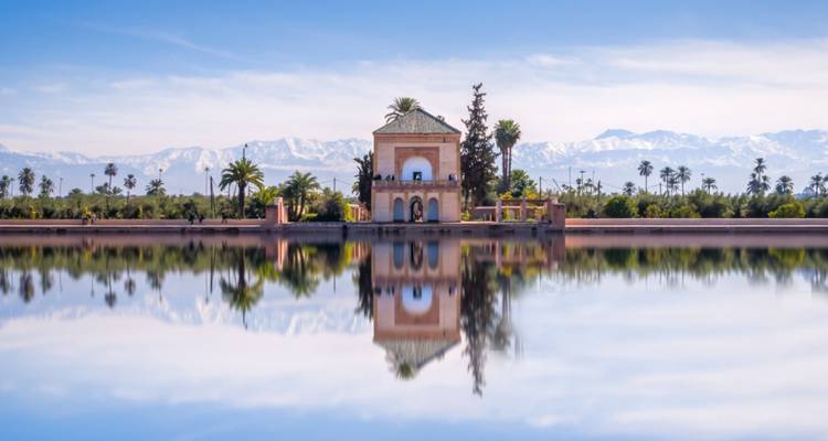 Pavillon serein parfaitement reflété dans le bassin des jardins de la Ménara avec les montagnes de l'Atlas enneigées en arrière-plan.