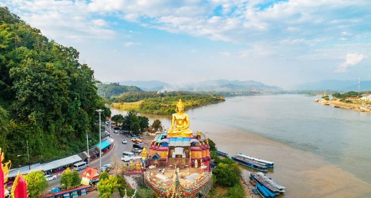 Large golden Buddha statue by the river with scenic views.