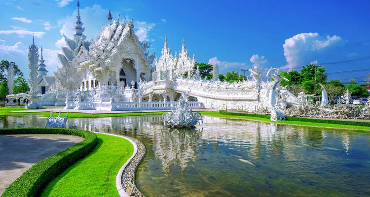 White ornate temple with gardens and reflection in a pond.