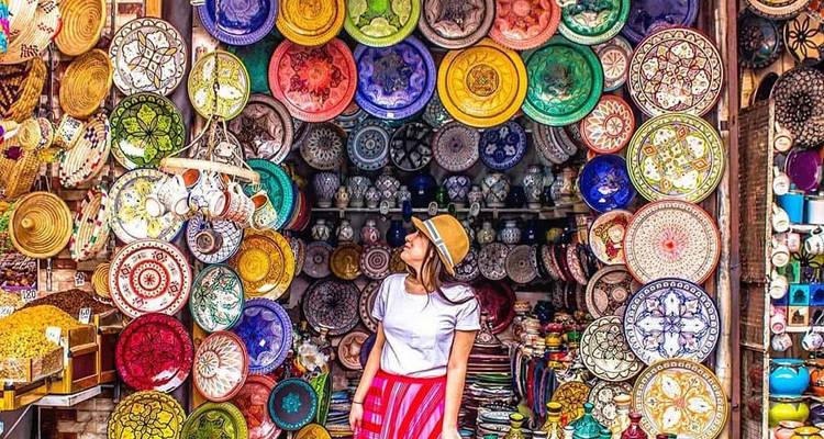 Una mujer admirando una colorida exhibición de platos de cerámica marroquíes tradicionales en un concurrido puesto del mercado.